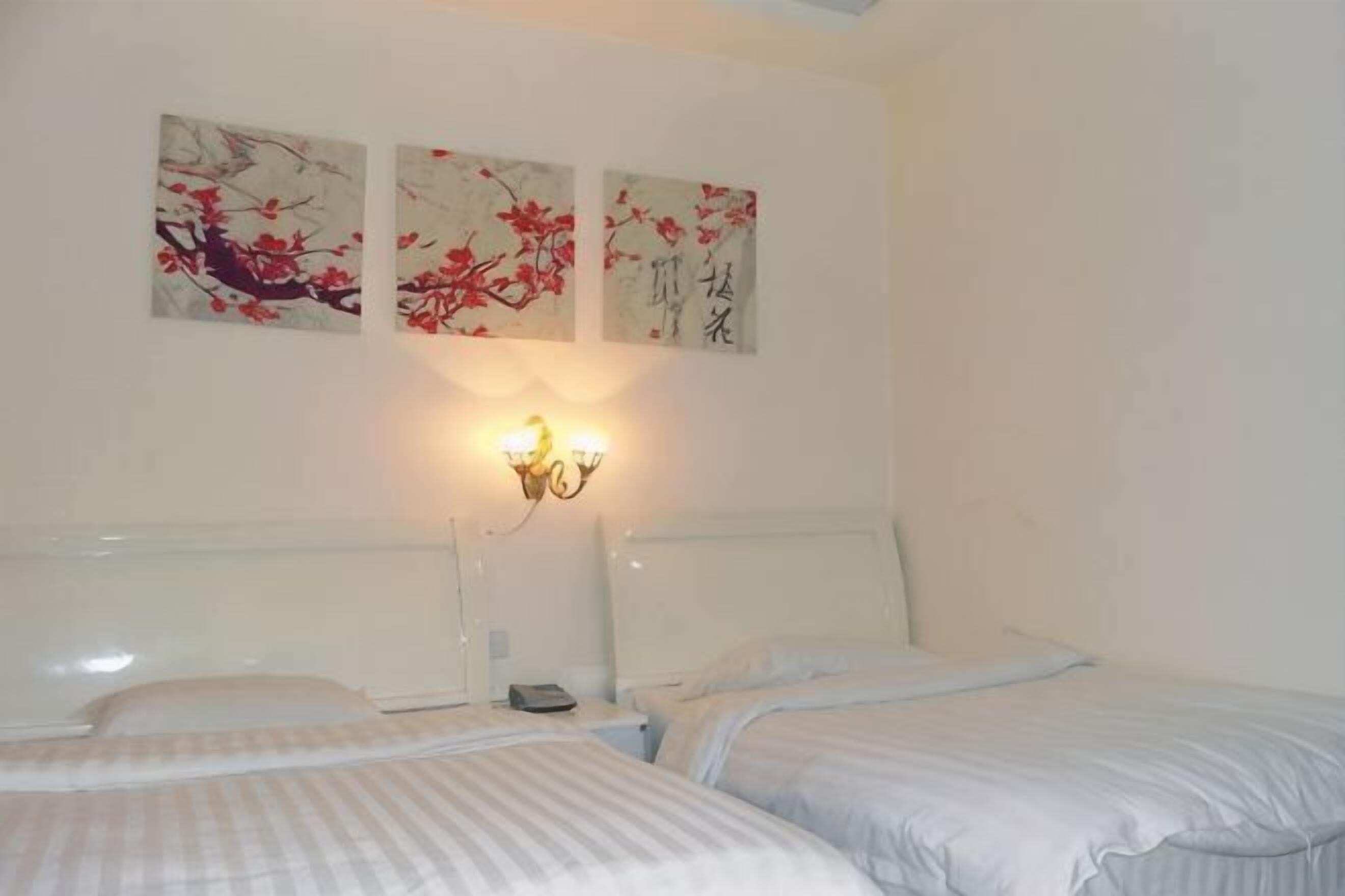 A bedroom with two beds, a nightstand, a wall-mounted lamp, and three wall art pieces.