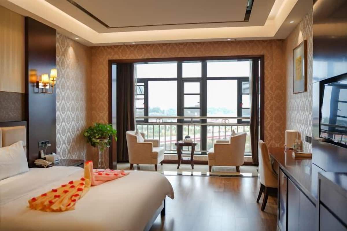 Habitación de hotel con cama, escritorio, dos sillas, una mesita, una planta y un ventanal con vistas.