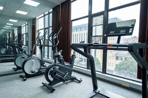 Un gimnasio con equipamiento de ejercicio, ventanas amplias y vistas a edificios.