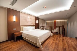 Habitación de hotel con una cama grande, suelo de madera, un escritorio, una silla y vistas al exterior a través de una ventana.