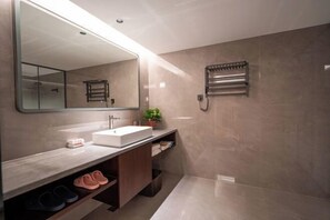 Un baño moderno con un espejo grande, un lavabo blanco, un perchero para toallas y una zona de ducha.
