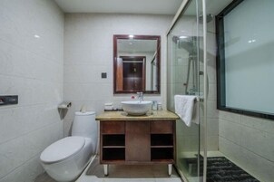 Un baño moderno con inodoro blanco, tocador de madera con lavamanos y cabina de ducha de vidrio.