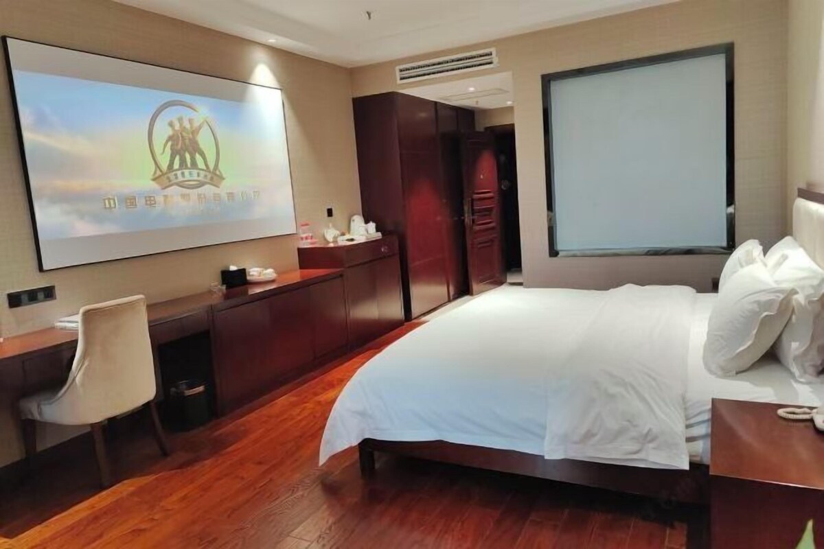 Habitación de hotel con cama, escritorio, silla, armario y televisor mostrando un logotipo.