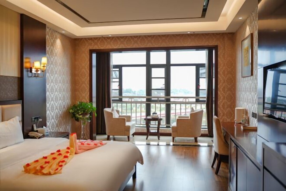 Habitación de hotel con una cama grande, un escritorio, dos sillas, una mesita y un ventanal con vistas.