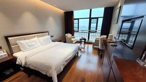 Una habitación de hotel moderna con una cama grande, un balcón con asientos y vistas a la ciudad.
