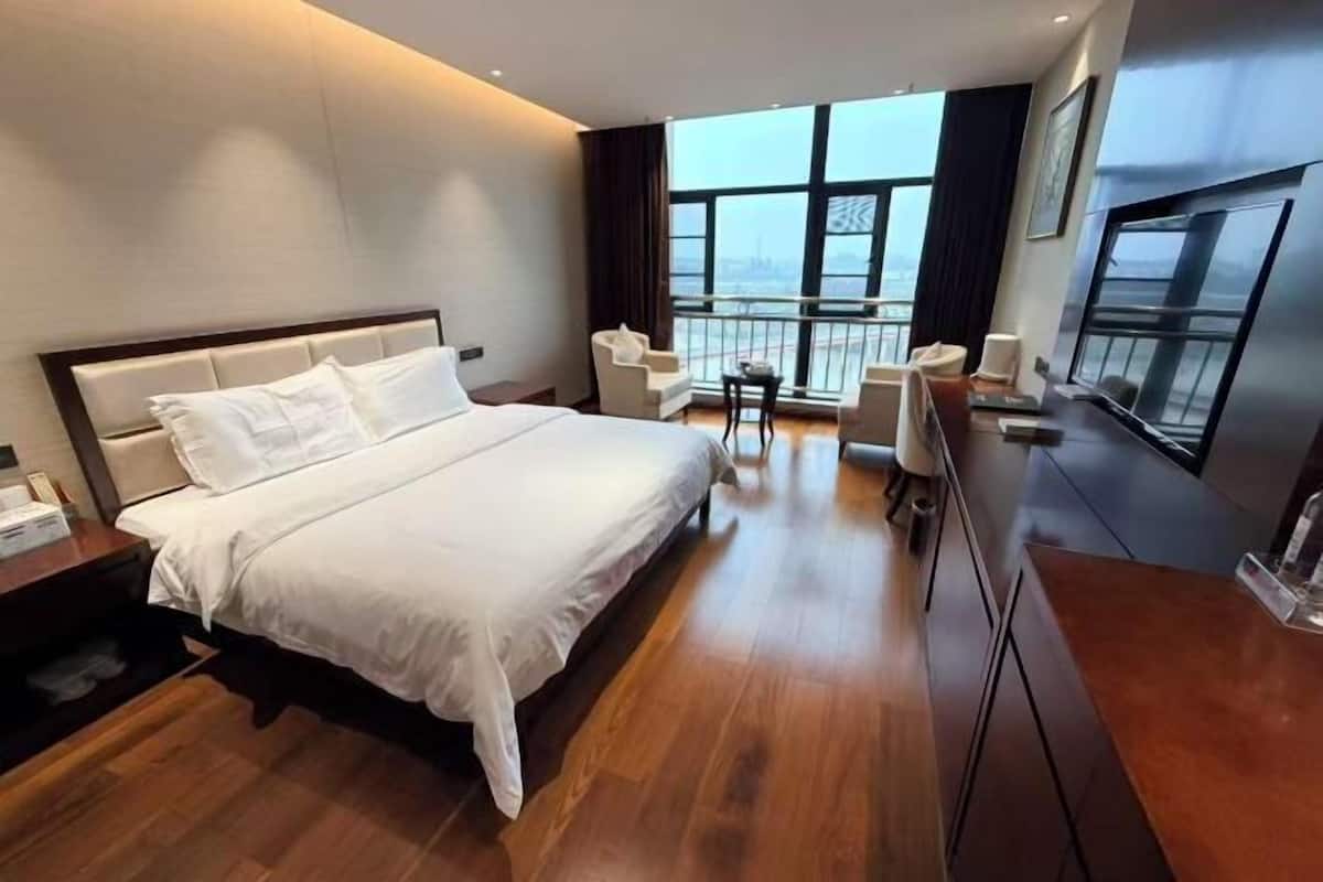 Una habitación de hotel moderna con una cama grande, un balcón con asientos y vistas a la ciudad.