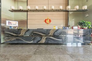 A reception desk with a marble top, a red decorative emblem, and a shelf with rolled towels.