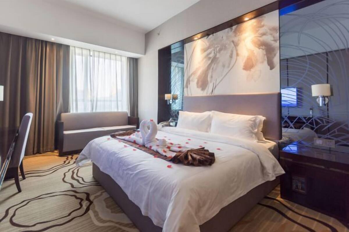 Una camera d'hotel con un letto, una scrivania, una sedia e un grande quadro astratto appeso alla parete.