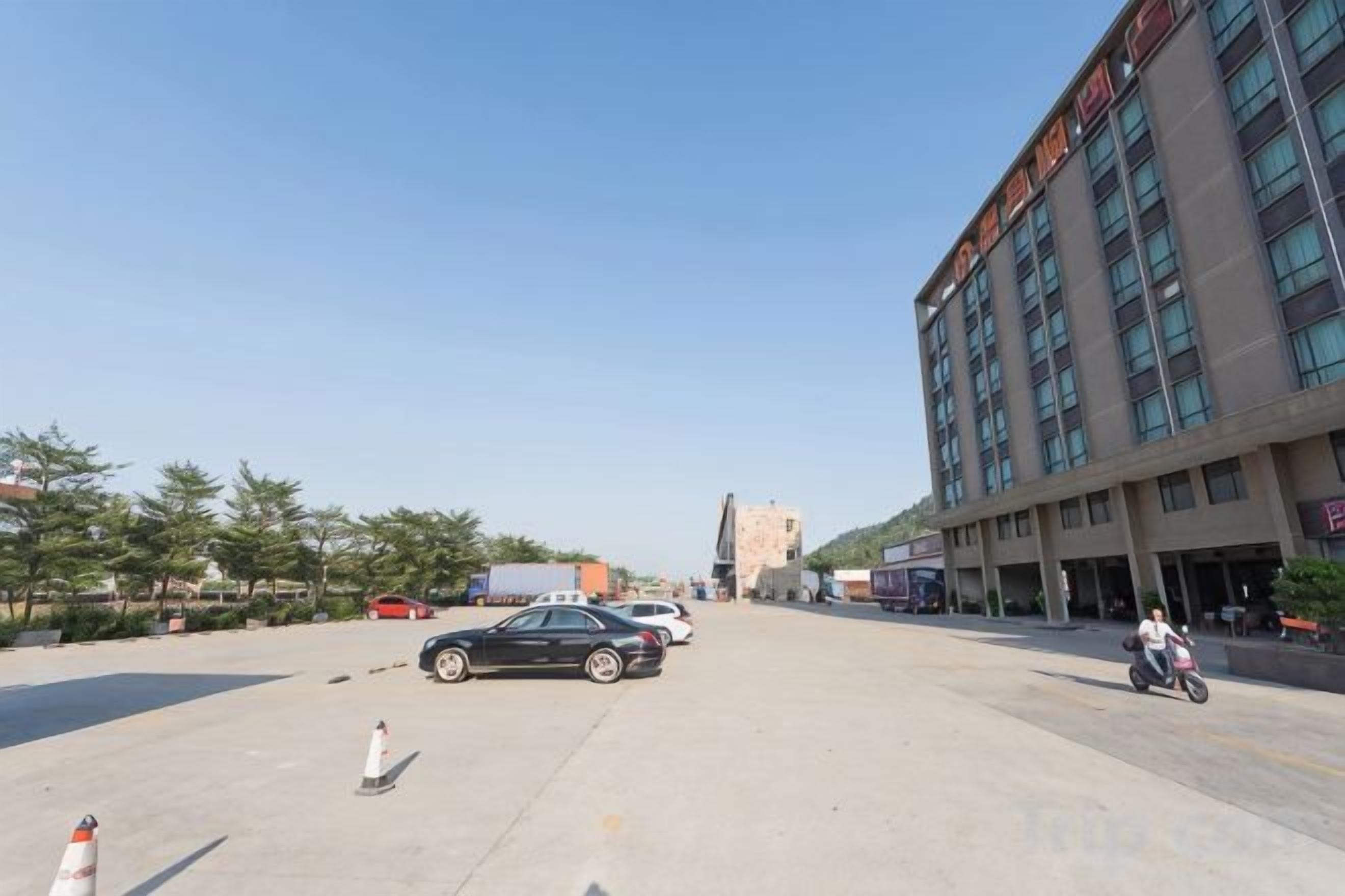 Un estacionamiento con un edificio al fondo, algunos coches y una motocicleta.
