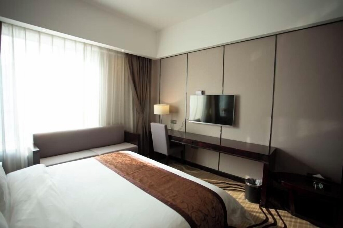 Une chambre d’hôtel avec un grand lit, un bureau, une chaise, une télévision et une fenêtre avec des rideaux.
