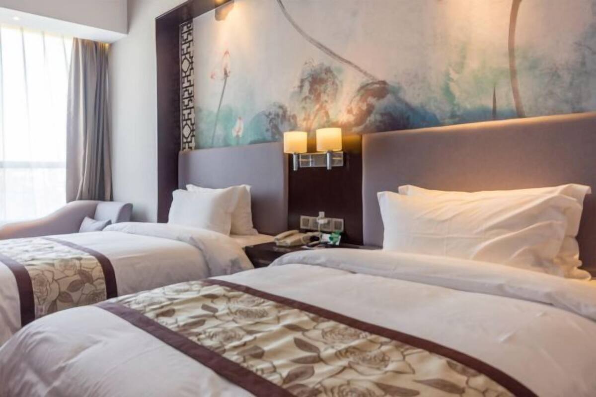 Una camera d'albergo con due letti, un comodino con un telefono e una parete decorata con un quadro.