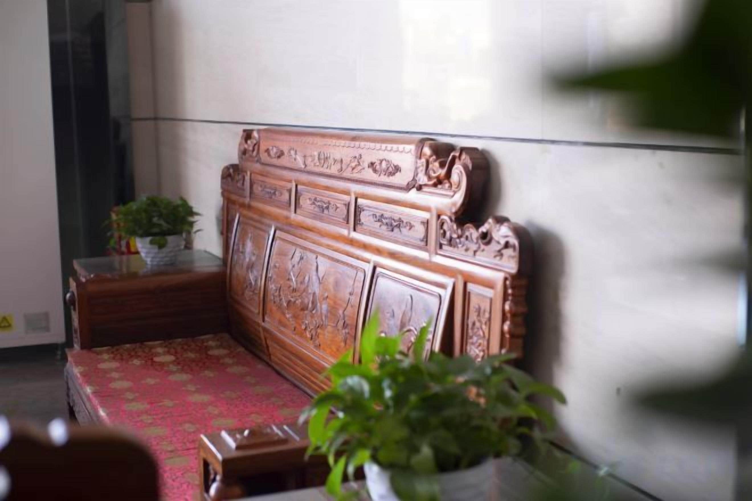 A wooden bench with intricate carvings, a potted plant, and a red patterned cushion.