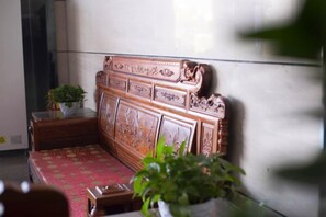 A wooden bench with intricate carvings, a potted plant, and a red patterned cushion. - Yi Jia Hotel (Zhuhai)
