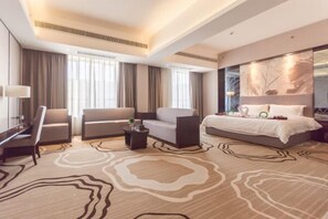 A modern hotel room with a large bed, two sofas, a desk, and a patterned carpet. - Yi Jia Hotel (Zhuhai)