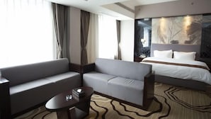 A modern hotel room with a sofa, a small table, a bed, and a large window with curtains. - Yi Jia Hotel (Zhuhai)