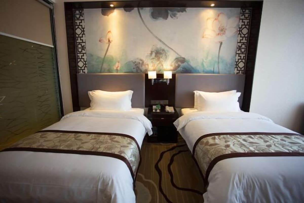 Une chambre d’hôtel avec deux lits, une table de chevet et un mur décoratif orné de motifs floraux.