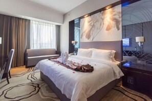 Une chambre d’hôtel avec un grand lit, un canapé, un bureau et un grand tableau abstrait accroché au mur.