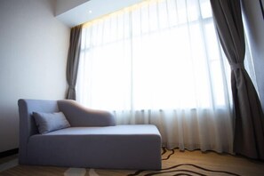 Un salon moderne avec un canapé, une grande fenêtre avec des rideaux et un tapis à motifs.