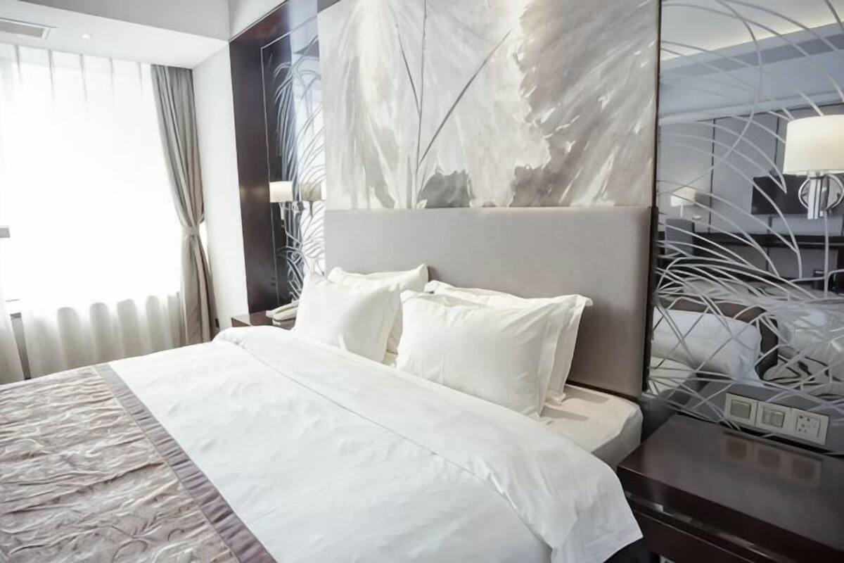 Una camera d'albergo con un letto grande, una testiera, un comodino e uno specchio.
