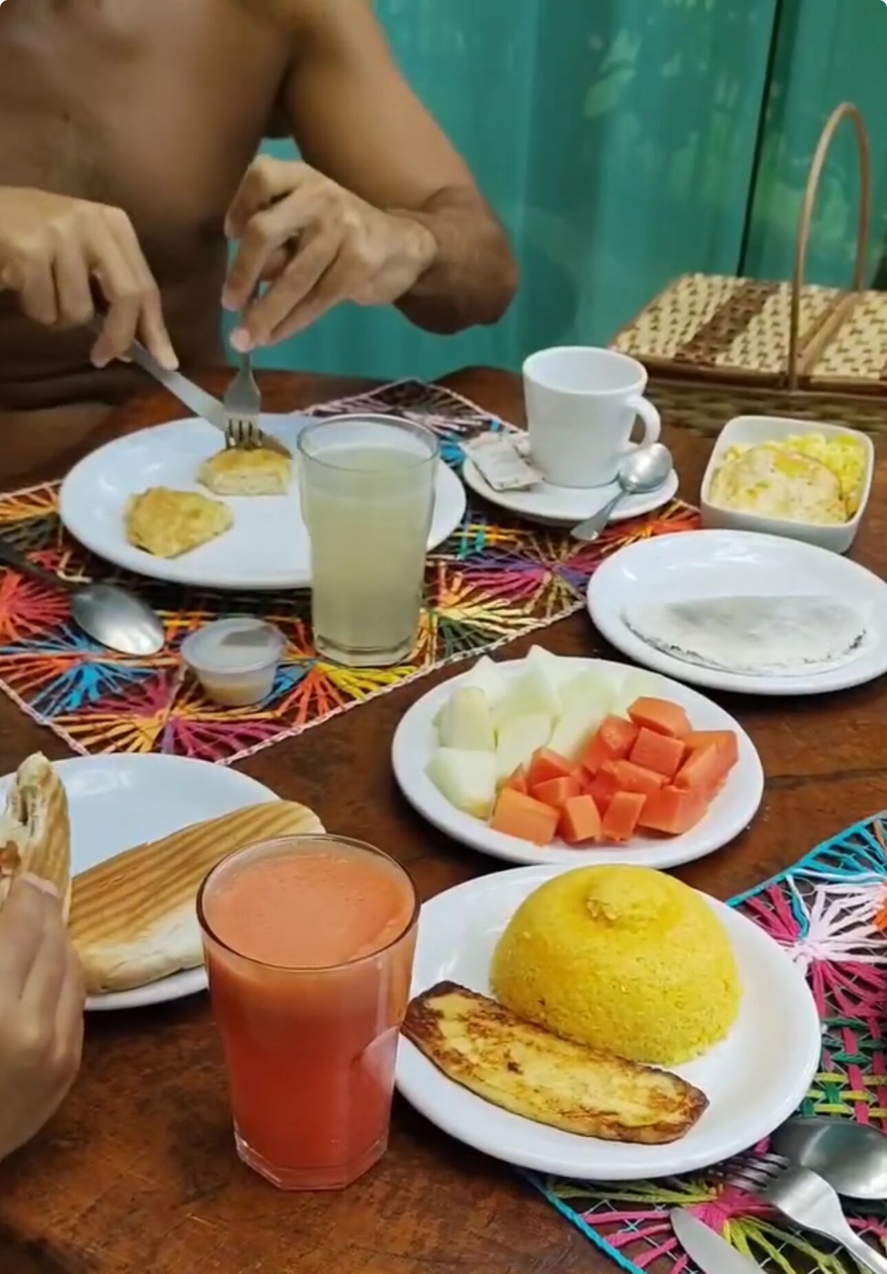 A table set with various dishes including a plate of fruit, a glass of juice, and a plate of yellow rice.