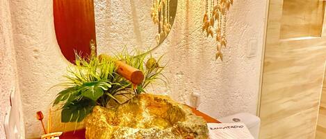 A bathroom with a wooden vanity, a mirror, a sink with a decorative rock, a hanging light fixture, and a toilet.