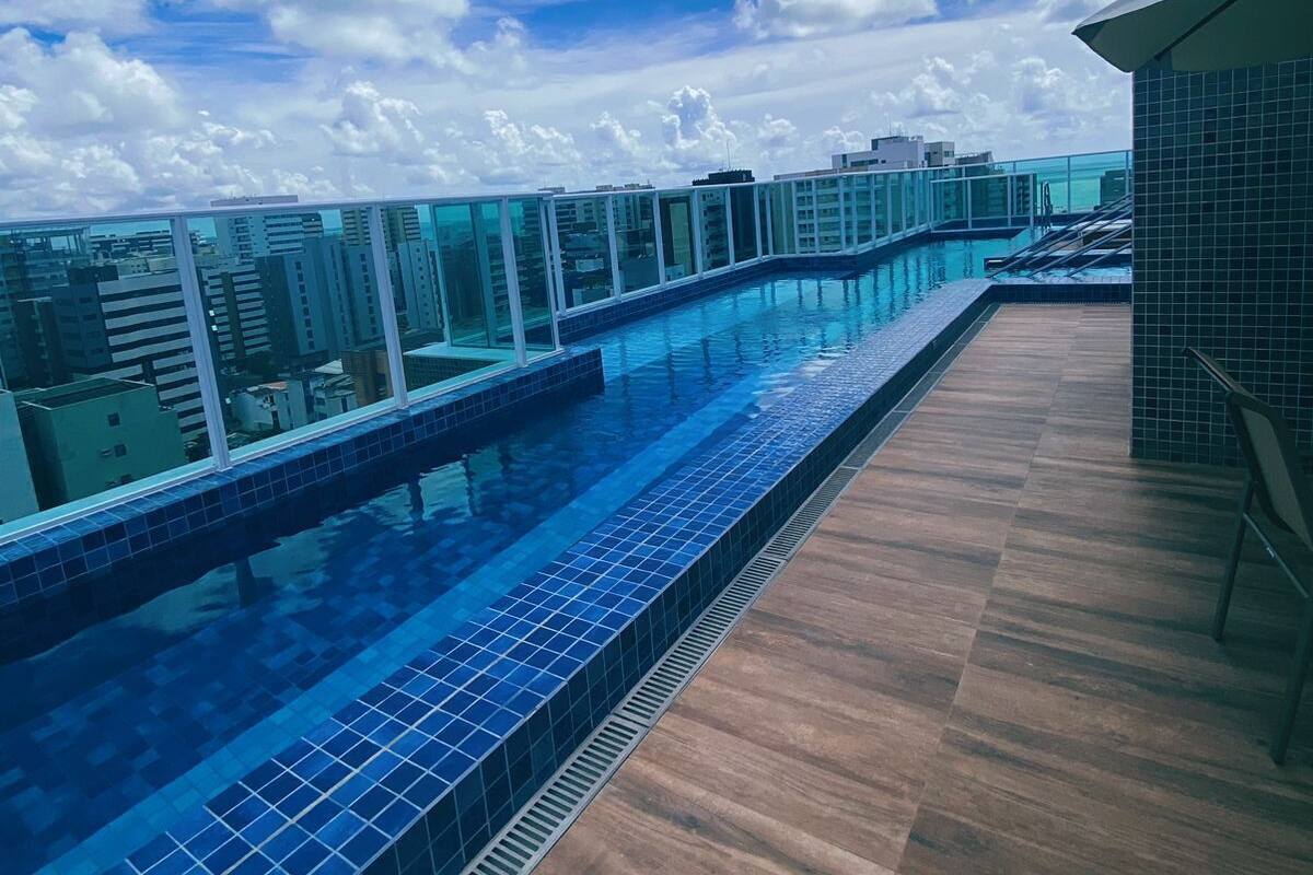 A rooftop pool with clear blue water, surrounded by a wooden deck and glass railings.
