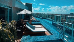 Un área de piscina en la azotea con sillones de descanso y una planta en maceta.