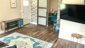 A living room with a wooden floor, a blue patterned rug, a sofa, a coffee table, a TV, and a brick wall. - Unique downtown Fruita apartment with bike storage! (Fruita)