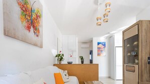 A modern living room with a white sofa, a wooden coffee table, and a cabinet. There is a colorful abstract painting on the wall and a potted plant on the coffee table. - Apartment Krempy - Two Bedroom Apartment with Terrace (Trogir)