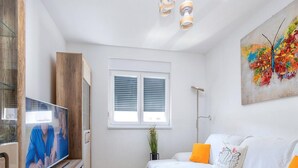 A modern living room with a TV, sofa, coffee table, and a window with blinds. - Apartment Krempy - Two Bedroom Apartment with Terrace (Trogir)