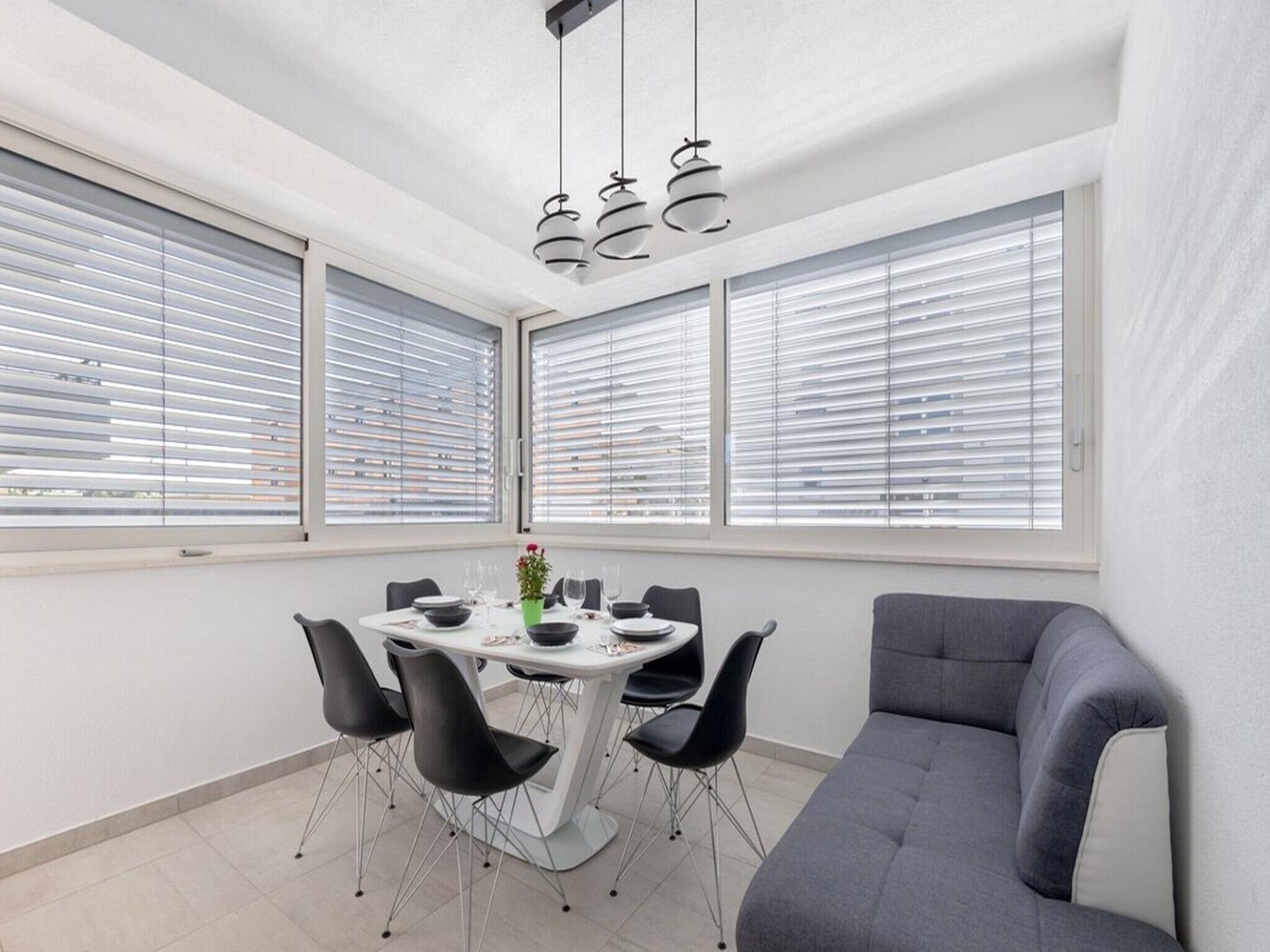 Uma zona de refeições moderna com uma mesa redonda, cadeiras pretas e um sofá cinzento.