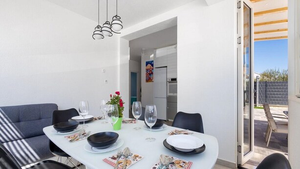 A modern dining area with a white table set for four, black chairs, and a black ceiling light fixture. - Apartment Krempy - Two Bedroom Apartment with Terrace (Trogir)