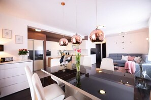 Una cocina moderna con electrodomésticos de acero inoxidable, una zona de comedor con mesa de vidrio y una sala de estar con sofá gris.