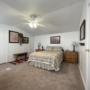A bedroom with a bed, two nightstands, a ceiling fan, and a bench.