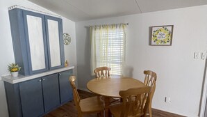 Un coin repas avec une table et des chaises en bois, un meuble bleu orné d’une plante, et une fenêtre avec des rideaux.
