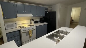 Une cuisine de taille réduite, dotée de plans de travail blancs, d’une cuisinière, d’un four à micro-ondes, d’un réfrigérateur et d’un évier.