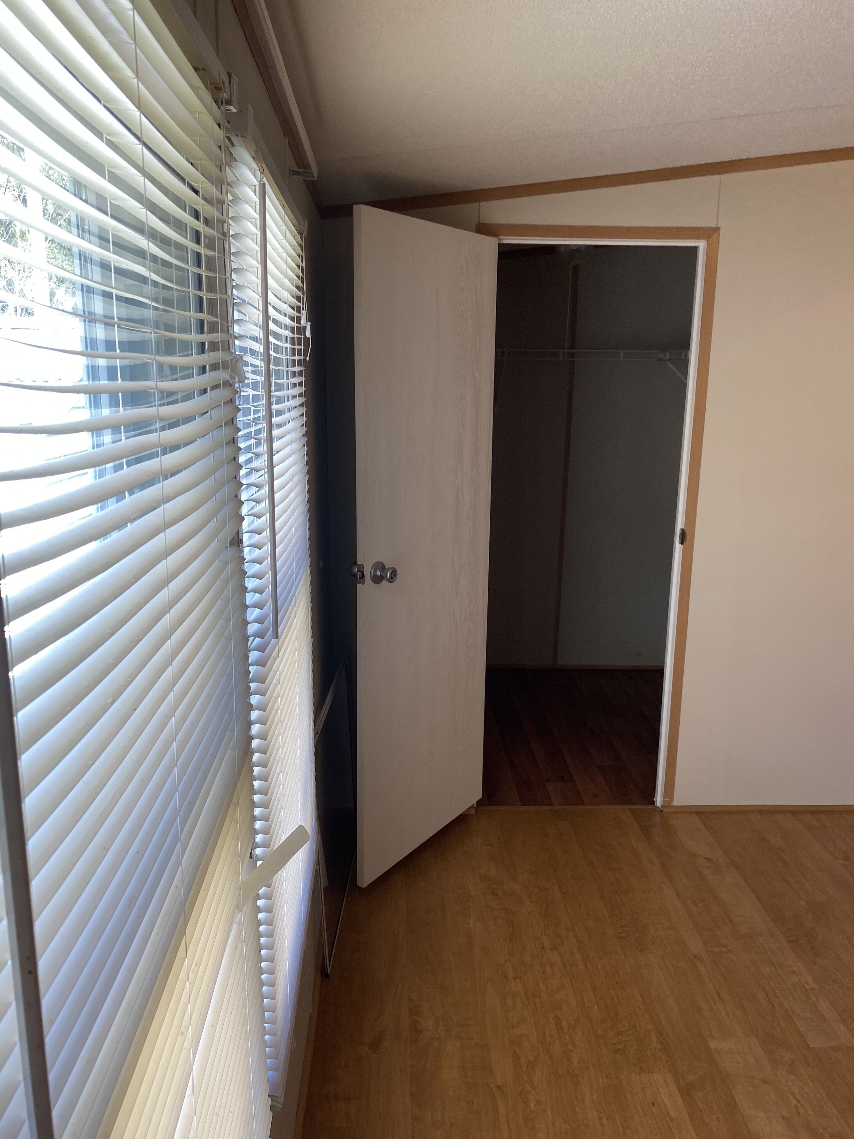 Ein Zimmer mit Holzboden, einer weißen Tür und einem Fenster mit Jalousien.