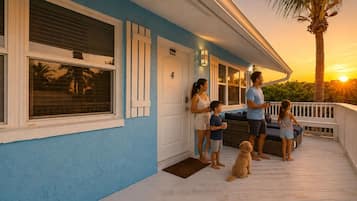 Une famille est assise sur le porche d’une maison, un chien est à leurs côtés, le numéro « 4 » est affiché sur la porte, et un coucher de soleil se dessine à l’arrière-plan.