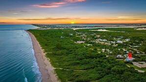An aerial view of a coastal area with a beach, dense greenery, and scattered buildings. - Surf Views 2BR - Sept Discounts Now Live! (Fort Pierce)