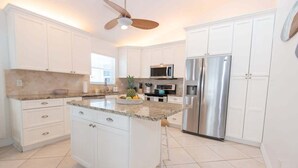 A modern kitchen with white cabinets, a stainless steel refrigerator, a microwave, and a granite countertop. - Surf Views 2BR - Sept Discounts Now Live! (Fort Pierce)