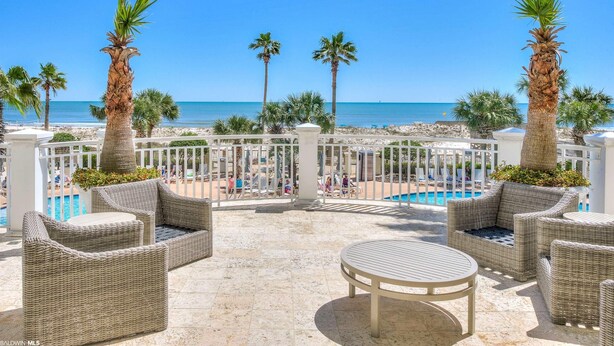 A terrace with wicker furniture, a pool, and palm trees overlooking the beach.