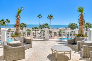 A terrace with wicker furniture, a pool, and palm trees overlooking the beach. - SNOWBIRD SALE!!  Discounted pricing for winter stays November through February! (Gulf Shores)