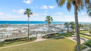 A beach view with palm trees, a wooden walkway, and a clear blue sky.