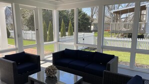 A sunroom with wicker furniture, a glass coffee table, and a view of a white picket fence and trees. - Walk to the Beach. Elevator.   Heated Pool Spa open from Mar 1-Oct 31 (Cape May)