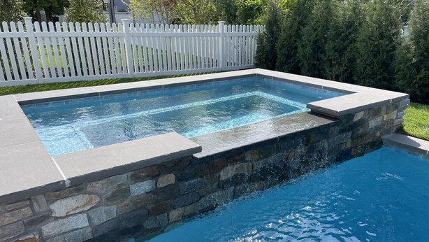 A rectangular swimming pool with a stone wall and a white picket fence in the background. - Walk to the Beach. Elevator.   Heated Pool Spa open from Mar 1-Oct 31 (Cape May)