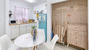 A compact kitchen with white cabinets, a microwave, a blue refrigerator, and a dining area with a white table and chairs. - Pineapple Shores Inn Unit 1 (Daytona Beach)