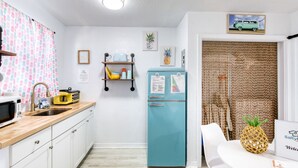 A compact kitchen with white cabinets, a wooden countertop, a blue refrigerator, and a small dining area with a white table and chairs. - Pineapple Shores Inn Unit 1 (Daytona Beach)
