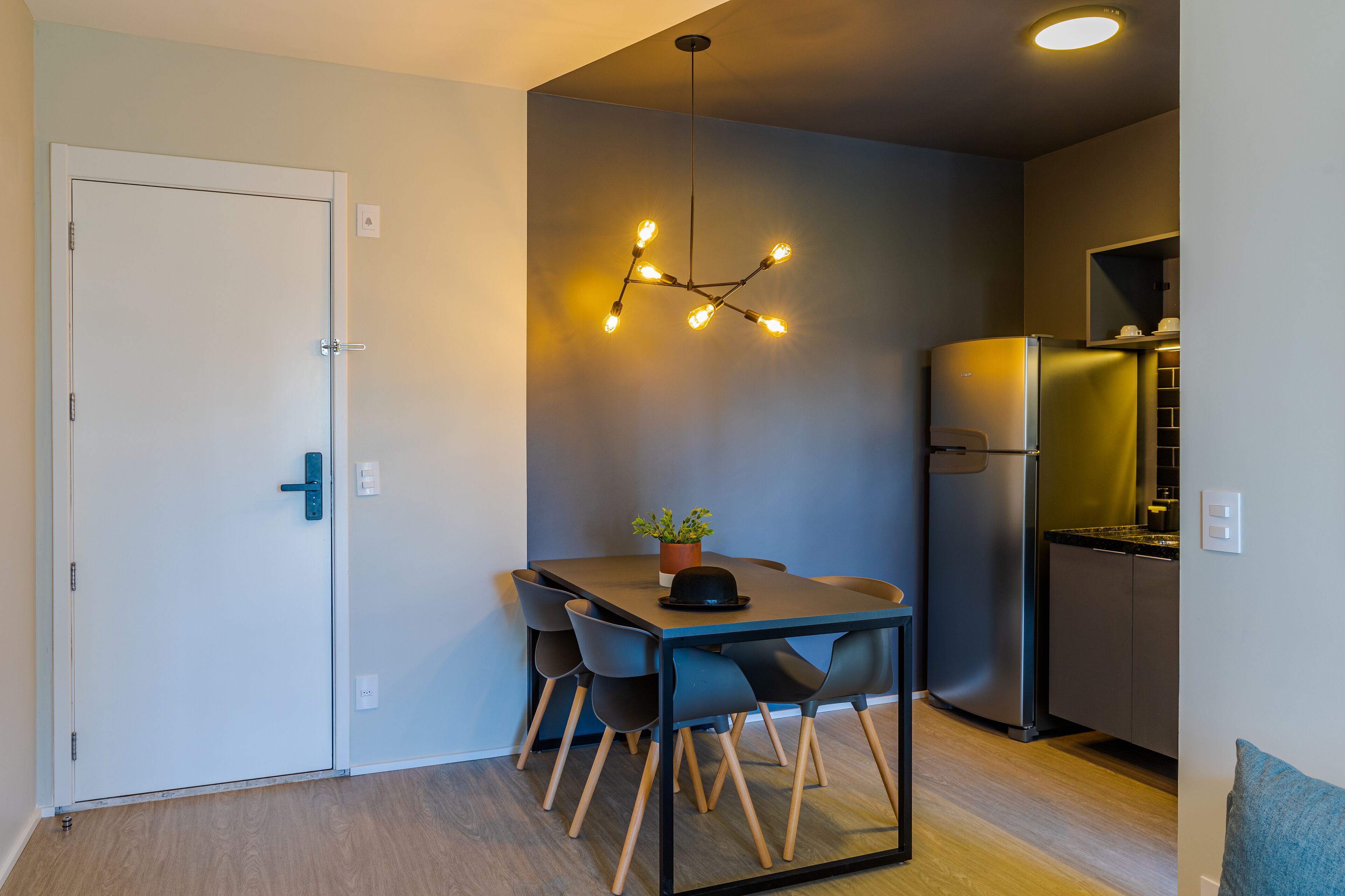 Μια σύγχρονη κουζίνα με εντοιχισμένο ψυγείο, μια τραπεζαρία με τραπέζι και καρέκλες και ένα φωτιστικό οροφής.