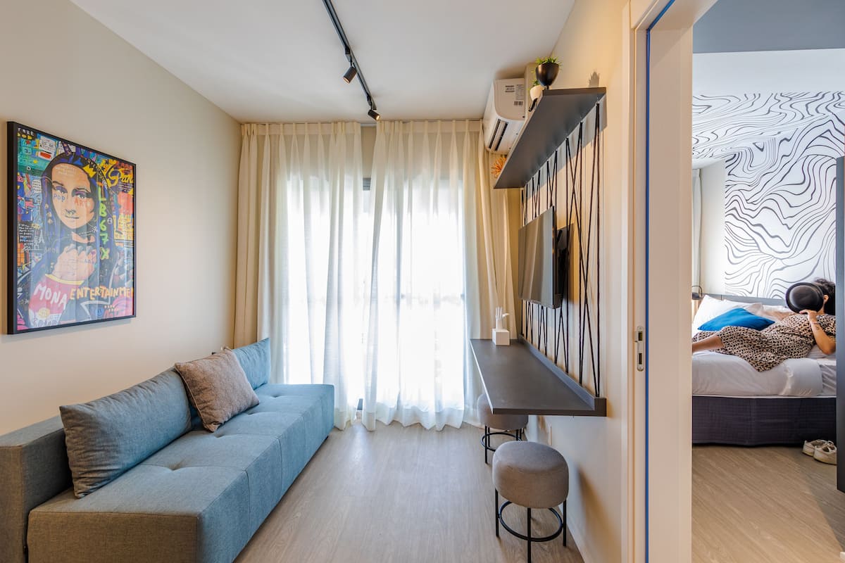 Een moderne kamer met een bank, een klein krukje, een bureau en een bed met een gestreept hoofdeinde.