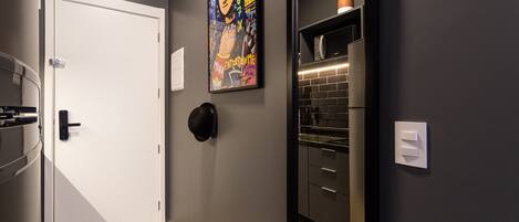 A hallway with a white door, a black wall, a colorful artwork, a black-framed mirror, and a potted plant on a shelf.